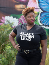 Load image into Gallery viewer, A Black woman with a TWA wearing a black v-neck t-shirt with the text &#39;#BlackWomenLead&#39; printed on the front.